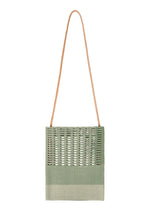 The MOKKO KNOT by GOOD GOODS ISSEY MIYAKE is a green rectangular knit shoulder bag featuring a textured woven flap and a long, thin tan strap, shown against a white background.