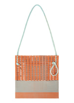 The MOKKO KNOT by GOOD GOODS ISSEY MIYAKE is a rectangular knit tote with an orange upper, light gray base, pale blue handles, and a side loop. Its open, airy design reflects modern minimalism.