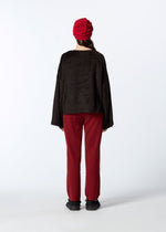 A person stands with their back to the camera, wearing HaaT’s SURI ALPACA textured red hat, a black jersey top, red pants, and black shoes against a plain white background inspired by Peru.