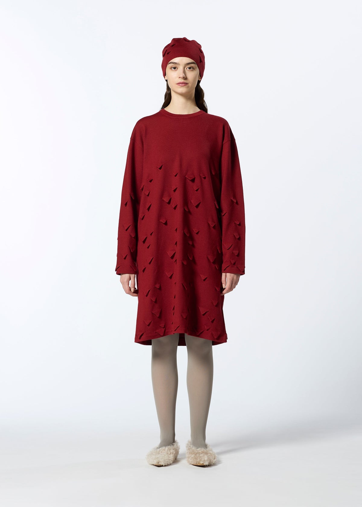 A woman faces forward against a white background, wearing the HaaT 3D△ KNIT textured red wool-blend dress with a matching red hat, light gray tights, and beige fluffy slippers. view 7 of 9