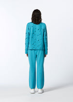 A person with curly hair faces away, wearing HaaT's 3D△ KNIT bright blue textured long-sleeved top and matching pants with white sneakers, set against a plain white background.