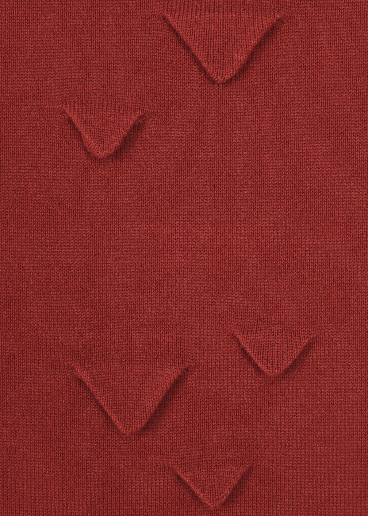 A close-up of HaaT’s 3D△ KNIT shows red wool-blend fabric with small, evenly spaced triangular folds formed by short-row knitting, creating a unique textured pattern. view 6 of 9
