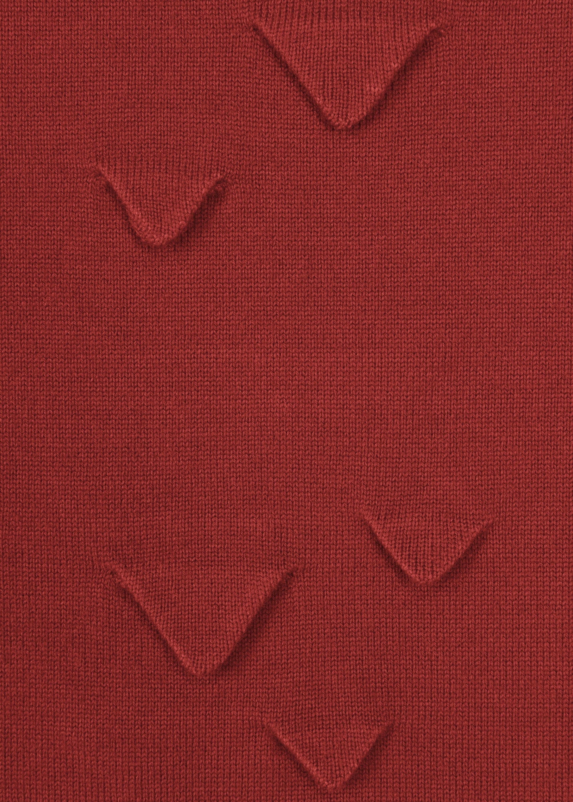 Zoomed view A close-up of HaaT’s 3D△ KNIT shows red wool-blend fabric with small, evenly spaced triangular folds formed by short-row knitting, creating a unique textured pattern.