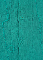 Close-up of teal KYO CHIJIMI EMB fabric by HaaT, showing vertical crinkles, two central round buttons, and irregular raised patterns for a soft, textured look.