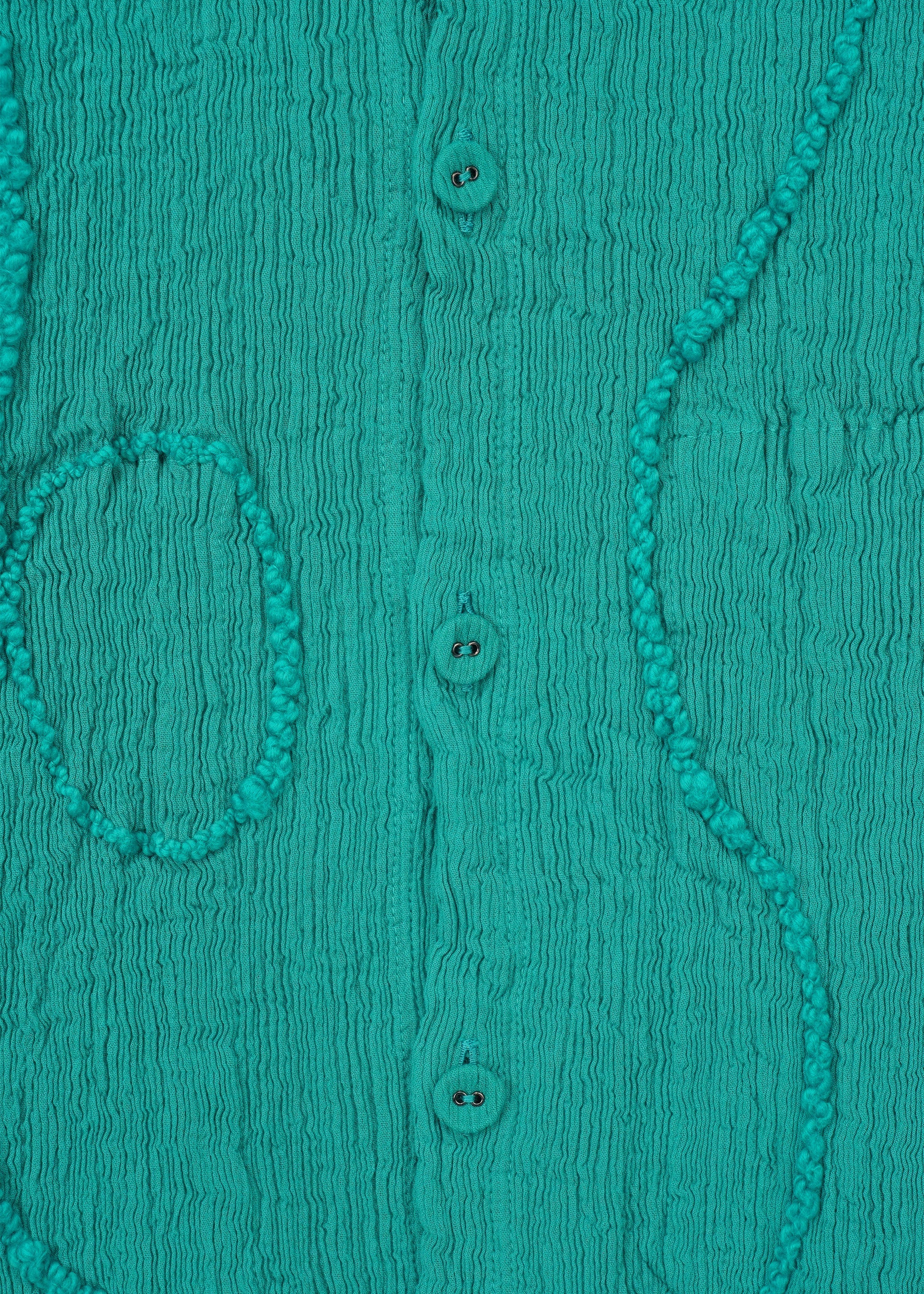 Zoomed view Close-up of HaaT's KYO CHIJIMI EMB jacket in teal, featuring vertical crinkles, three central buttons, and decorative raised stitched lines in wavy and oval embroidery-like patterns.