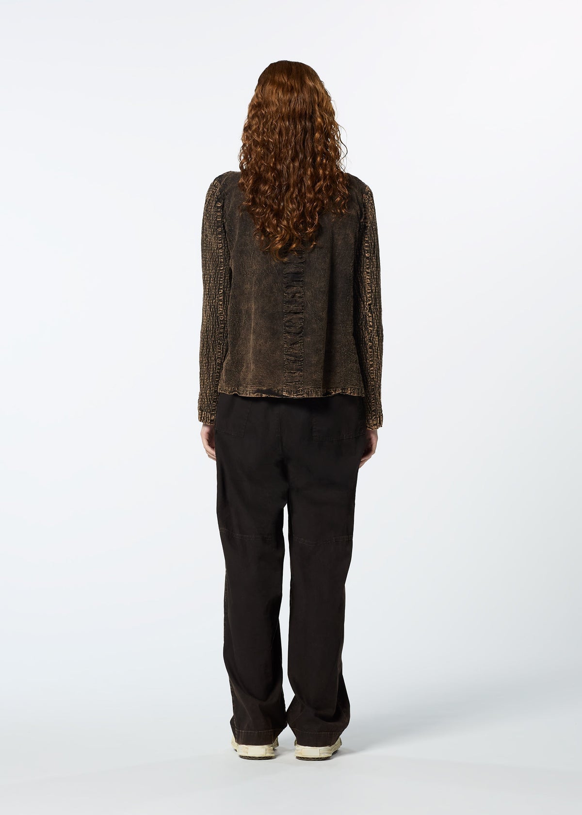 A person with long curly hair, dressed in HaaT’s TENMOKU COTTON top and loose black pants, stands facing away from the camera against a plain white background. view 8 of 9