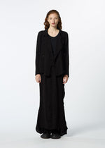 A woman with long wavy red hair stands facing forward, wearing the HaaT TENMOKU COTTON black textured blazer and long matching skirt, paired with black shoes, against a plain white background.