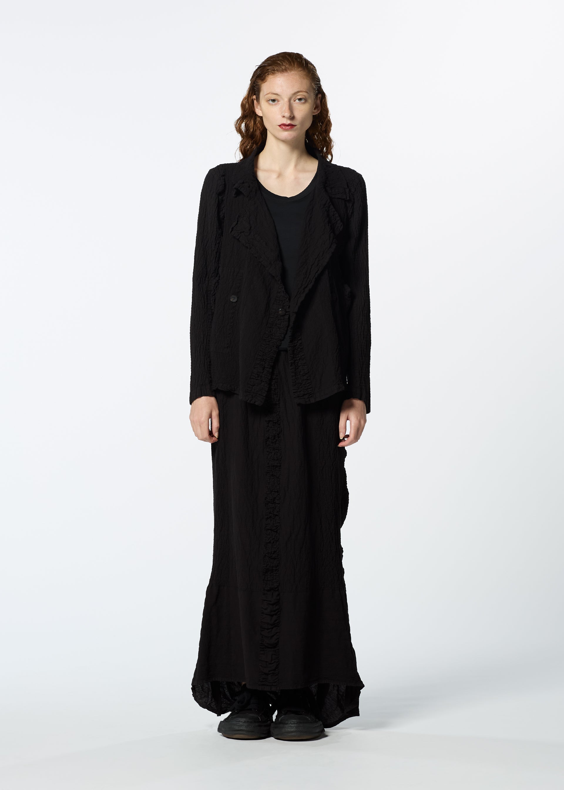 Zoomed view A woman with long wavy red hair stands facing forward, wearing the HaaT TENMOKU COTTON black textured blazer and long matching skirt, paired with black shoes, against a plain white background.