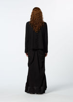 A person with long curly hair, wearing the HaaT TENMOKU COTTON loose garment-dyed black top and long black skirt, stands facing away against a plain white background.
