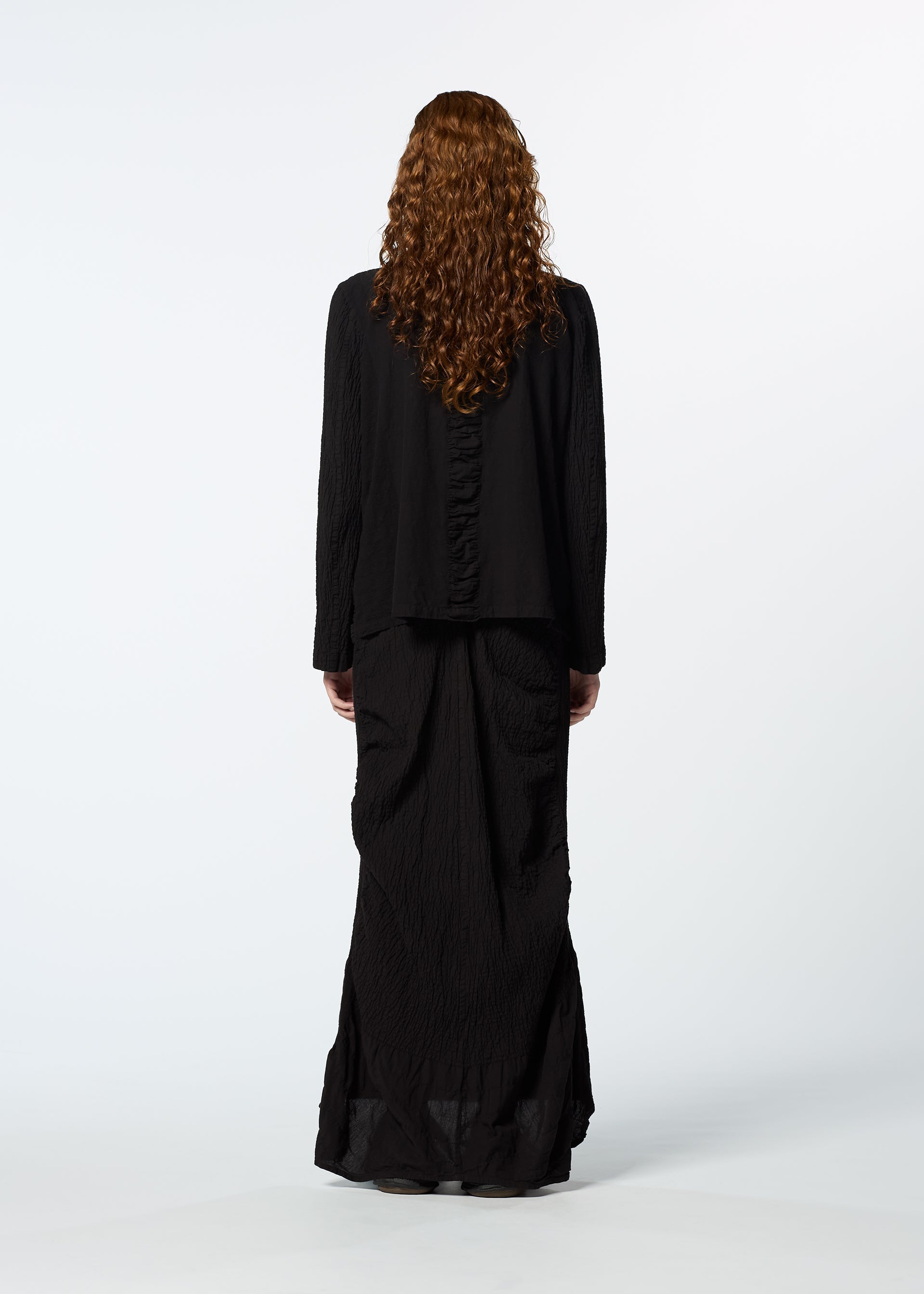 Zoomed view A person with long curly hair, wearing the HaaT TENMOKU COTTON loose garment-dyed black top and long black skirt, stands facing away against a plain white background.