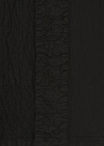 Close-up of black TENMOKU COTTON by HaaT, showing textured fabric with a crinkled pattern and a central vertical strip of tight ruching, echoing the intricate detailing of garment-dyed ceramics.