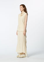 A woman with long, wavy hair poses in profile wearing HaaT's TENMOKU COTTON sleeveless cream garment-dyed top and matching long skirt with cream sneakers, set against a plain white background.
