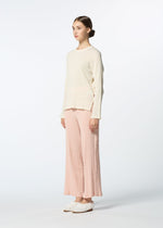 Against a plain white background, a person wears a cream long-sleeve top, HaaT KYO CHIJIMI FEBRUARY pants in light pink, and white textured shoes. Their hair is in a low bun, highlighting the ultra-fine cotton yarn’s refined look.