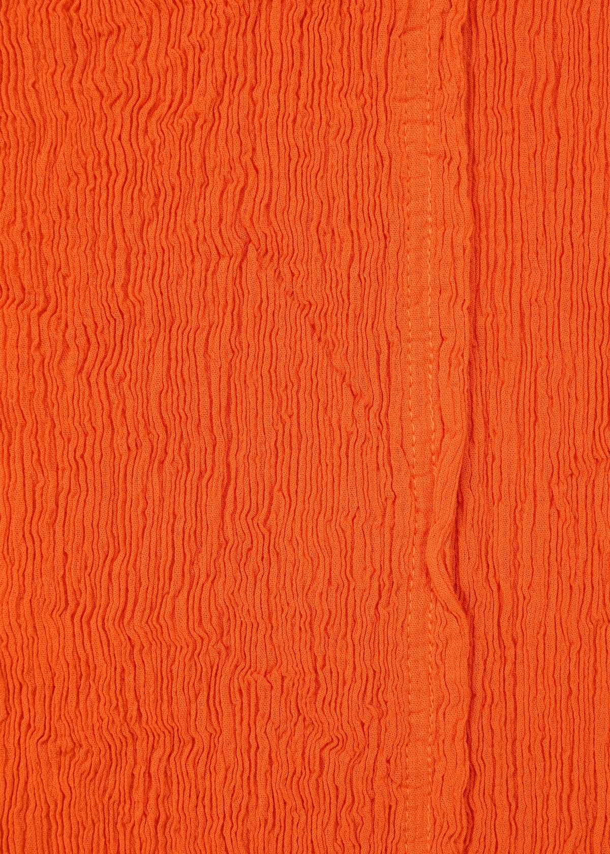 Close-up of textured orange fabric with vertical crinkles and a subtle seam, reminiscent of HaaT's KYO CHIJIMI MAY wide pants. Crafted from ultra-fine cotton yarn, the material has an uneven, wavy surface pattern. view 6 of 9