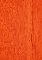 Close-up of textured orange fabric with vertical crinkles and a subtle seam, reminiscent of HaaT's KYO CHIJIMI MAY wide pants. Crafted from ultra-fine cotton yarn, the material has an uneven, wavy surface pattern.