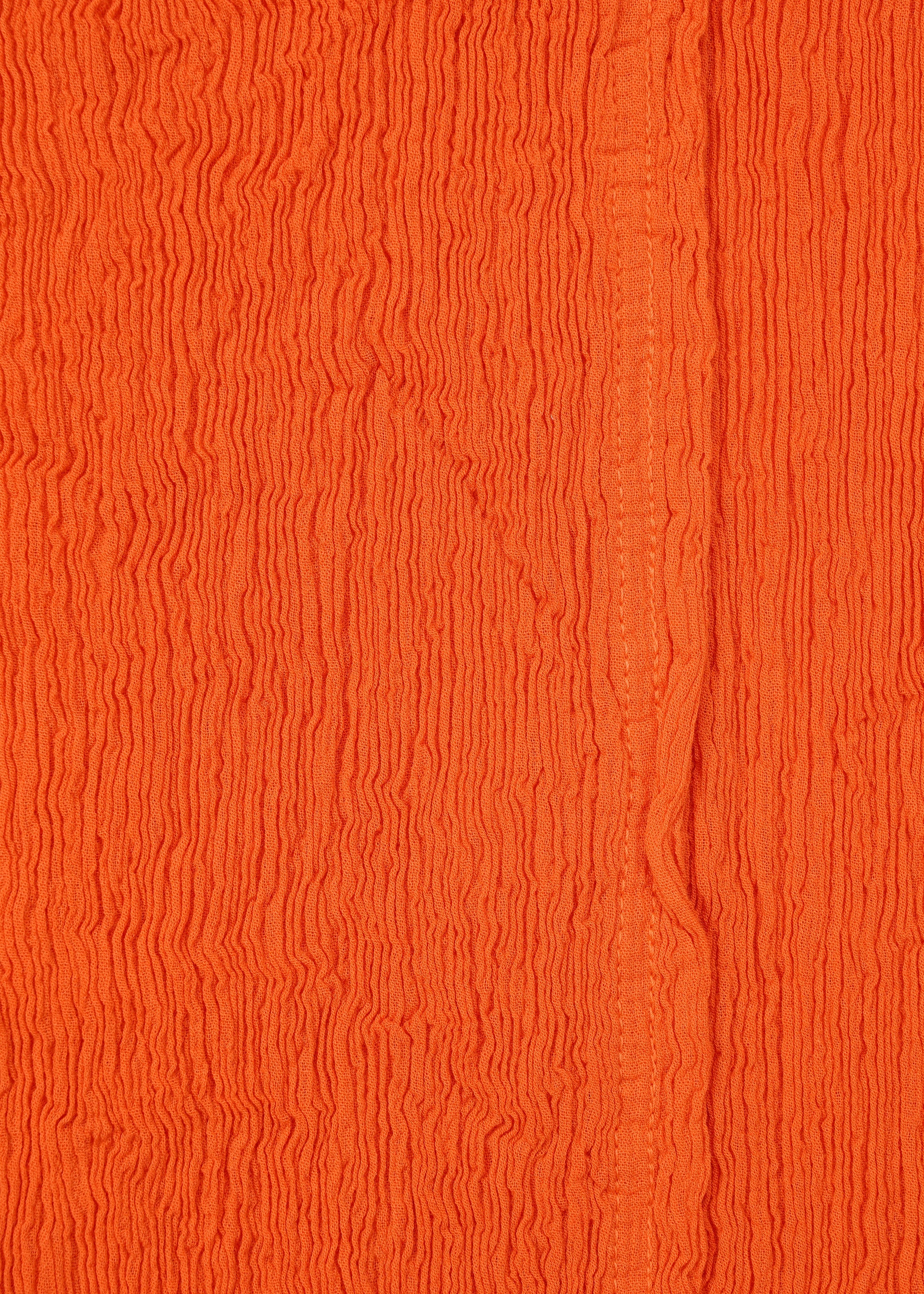 Zoomed view Close-up of textured orange fabric with vertical crinkles and a subtle seam, reminiscent of HaaT's KYO CHIJIMI MAY wide pants. Crafted from ultra-fine cotton yarn, the material has an uneven, wavy surface pattern.