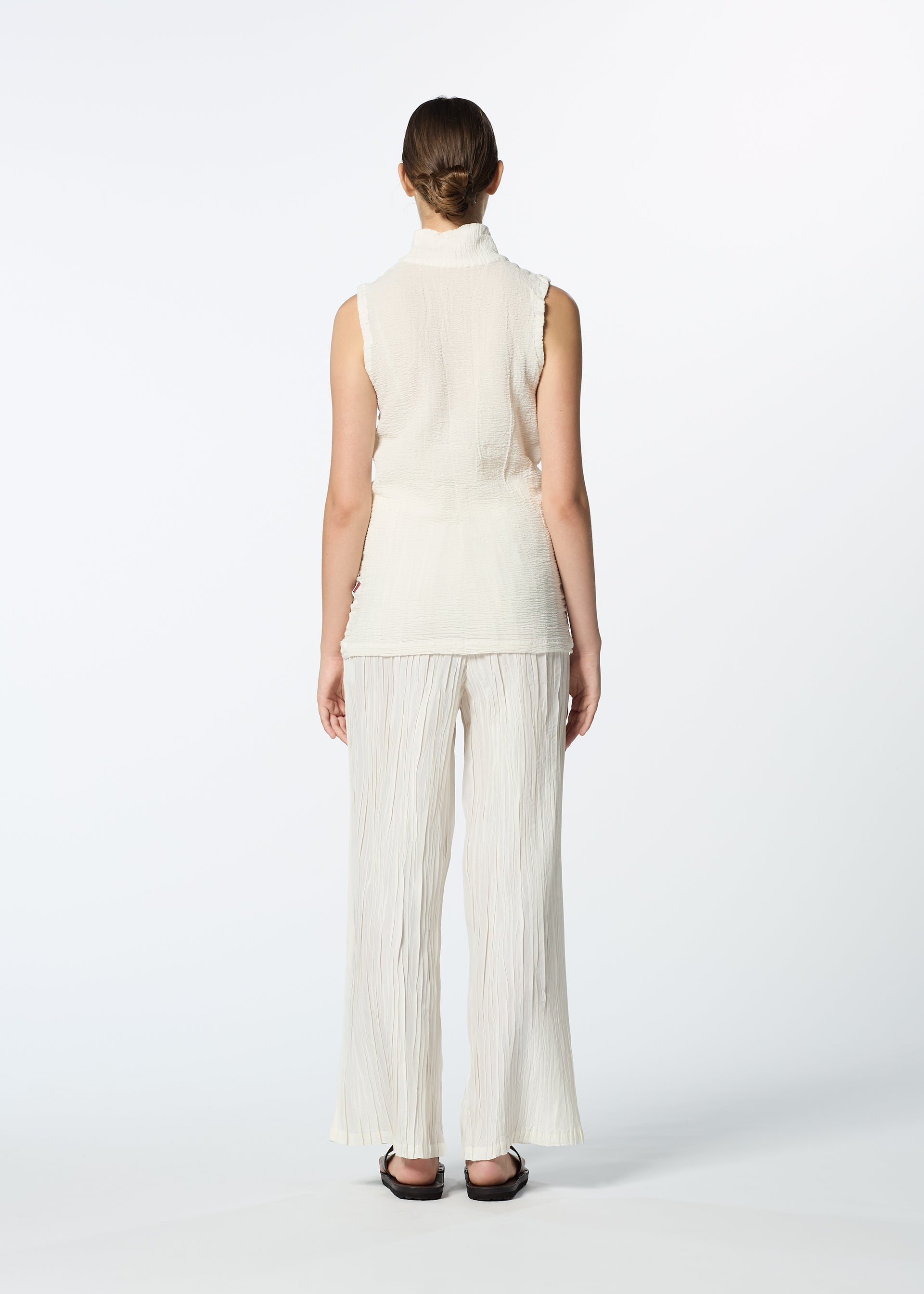 Zoomed view A woman, her hair tied back, wears HaaT’s SHIBARI BOTTOM—cream wide-legged pants—with a matching sleeveless hand-folded top and black sandals, standing against a plain white background.