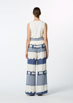 A person stands facing away, wearing HaaT's KASANEGAKE sleeveless white top and jacquard woven wide-leg pants with blue and white stripes, frayed edges, and varied texture, set against a plain white background.