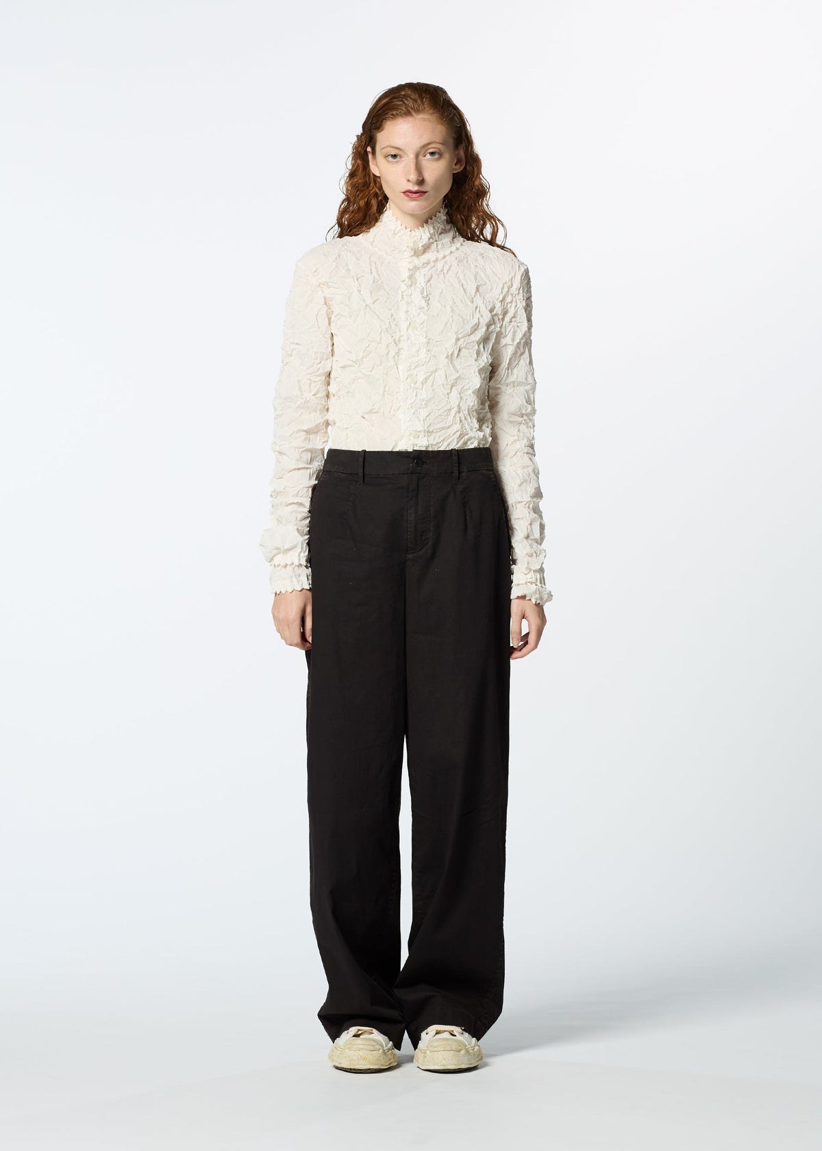 A person with long curly hair wears a textured white long-sleeve top, HaaT TENMOKU BOTTOM garment-dyed pants, and off-white sneakers, standing against a plain light background. view 6 of 8