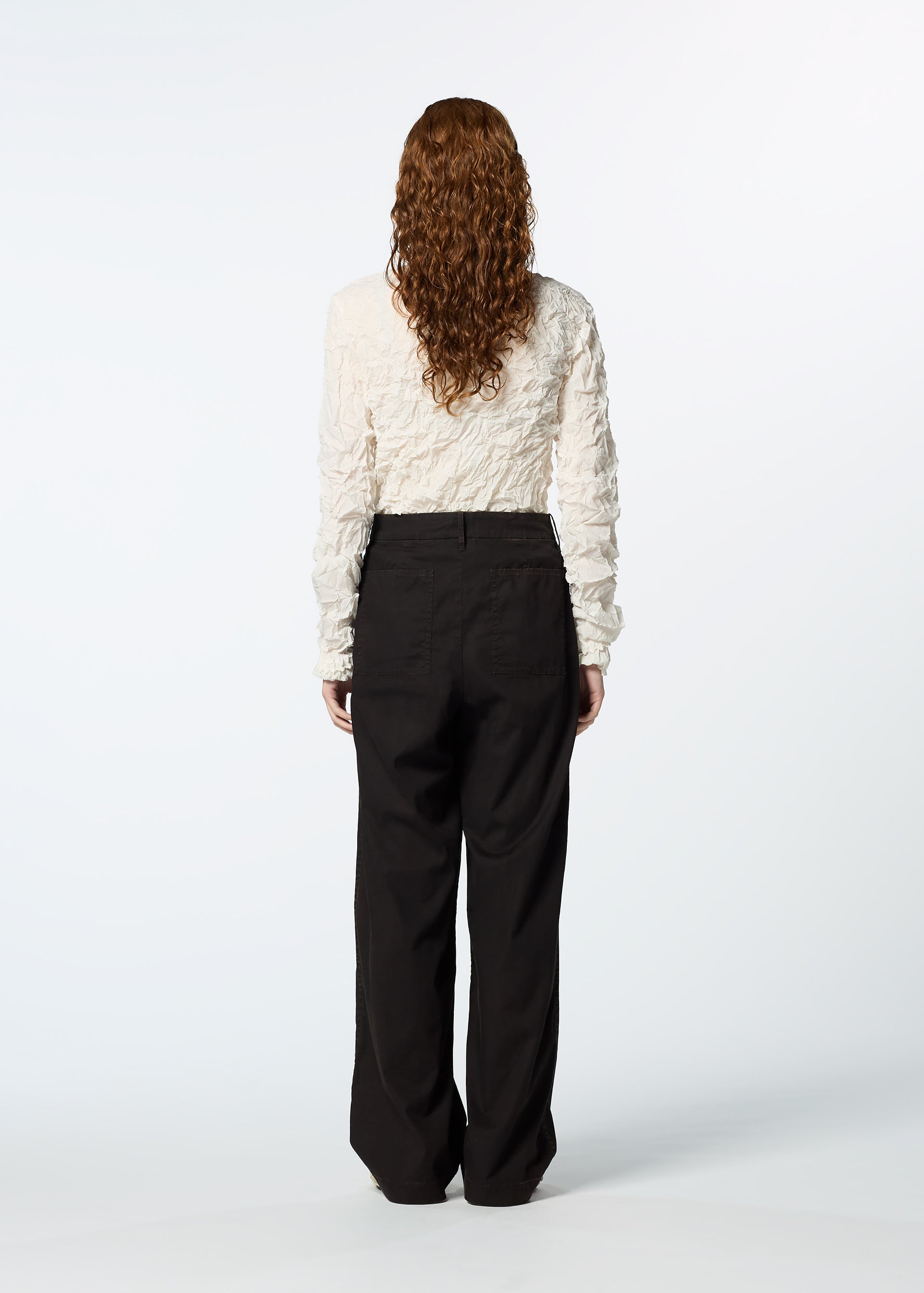 Zoomed view A person with long curly hair faces away, wearing a textured white long-sleeve top and HaaT TENMOKU BOTTOM loose-fitting pants against a plain white background.