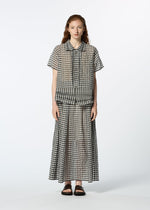 A person faces forward in a loose-fitting, short-sleeved HaaT 2 SIDE PINTUCKING black-and-white gingham button-up shirt, matching gingham skirt, and black sandals against a plain white background.