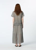 A person with long curly hair stands facing away, wearing HaaT's 2 SIDE PINTUCKING loose short-sleeved top and matching black-and-white gingham skirt with sandals, set against a plain light background.