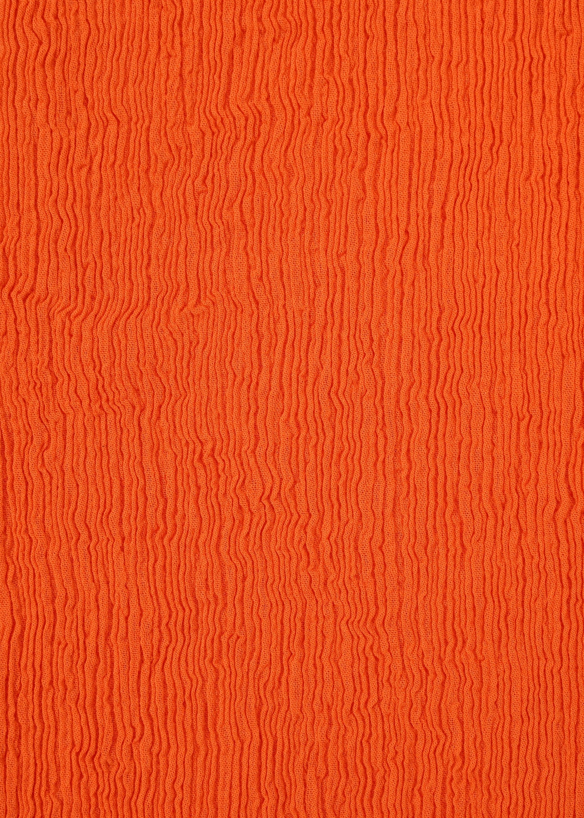 Close-up of an orange surface with wavy, vertical textured lines, evoking the rippled pattern of HaaT’s KYO CHIJIMI MAY skirt fabric, woven from ultra-fine cotton yarn on a unique loom. view 6 of 9