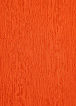Close-up of an orange surface with wavy, vertical textured lines, evoking the rippled pattern of HaaT’s KYO CHIJIMI MAY skirt fabric, woven from ultra-fine cotton yarn on a unique loom.
