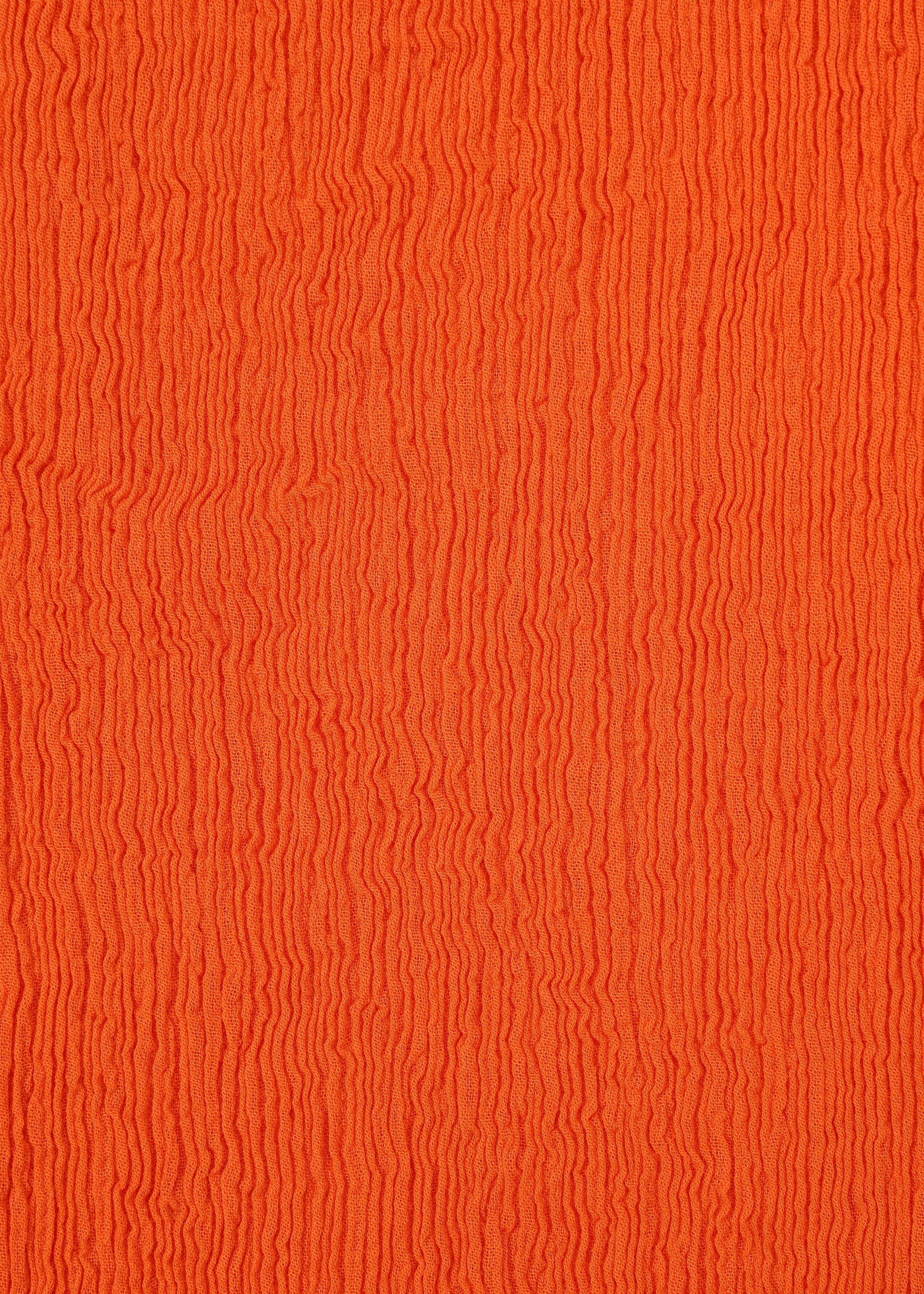 Zoomed view Close-up of an orange surface with wavy, vertical textured lines, evoking the rippled pattern of HaaT’s KYO CHIJIMI MAY skirt fabric, woven from ultra-fine cotton yarn on a unique loom.