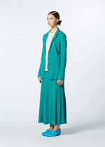 A woman stands against a plain background in a textured teal HaaT KYO CHIJIMI EMB blazer and matching skirt with a flared silhouette, cream top, and teal shoes. Her hair is tied back as she gazes slightly to the side with a neutral expression.