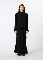 A person with long, wavy hair faces forward in a loose-fitting, long-sleeved black TENMOKU COTTON top and a garment-dyed textured skirt by HaaT, set against a plain white background.
