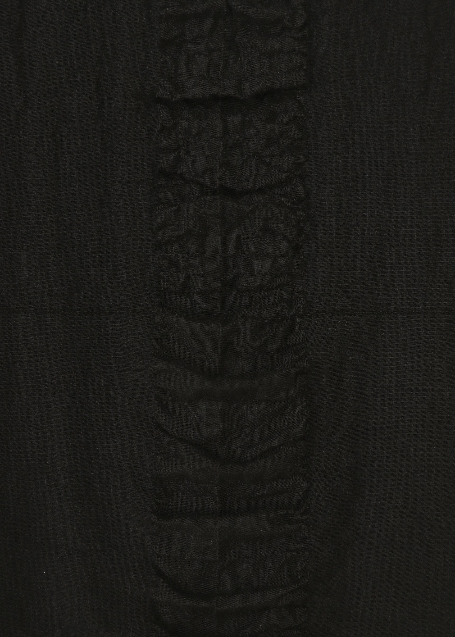 Zoomed view A close-up of HaaT’s TENMOKU COTTON skirt fabric features a garment-dyed, textured surface with a central vertical ruffle, highlighting rich textures and creases against a smooth background.