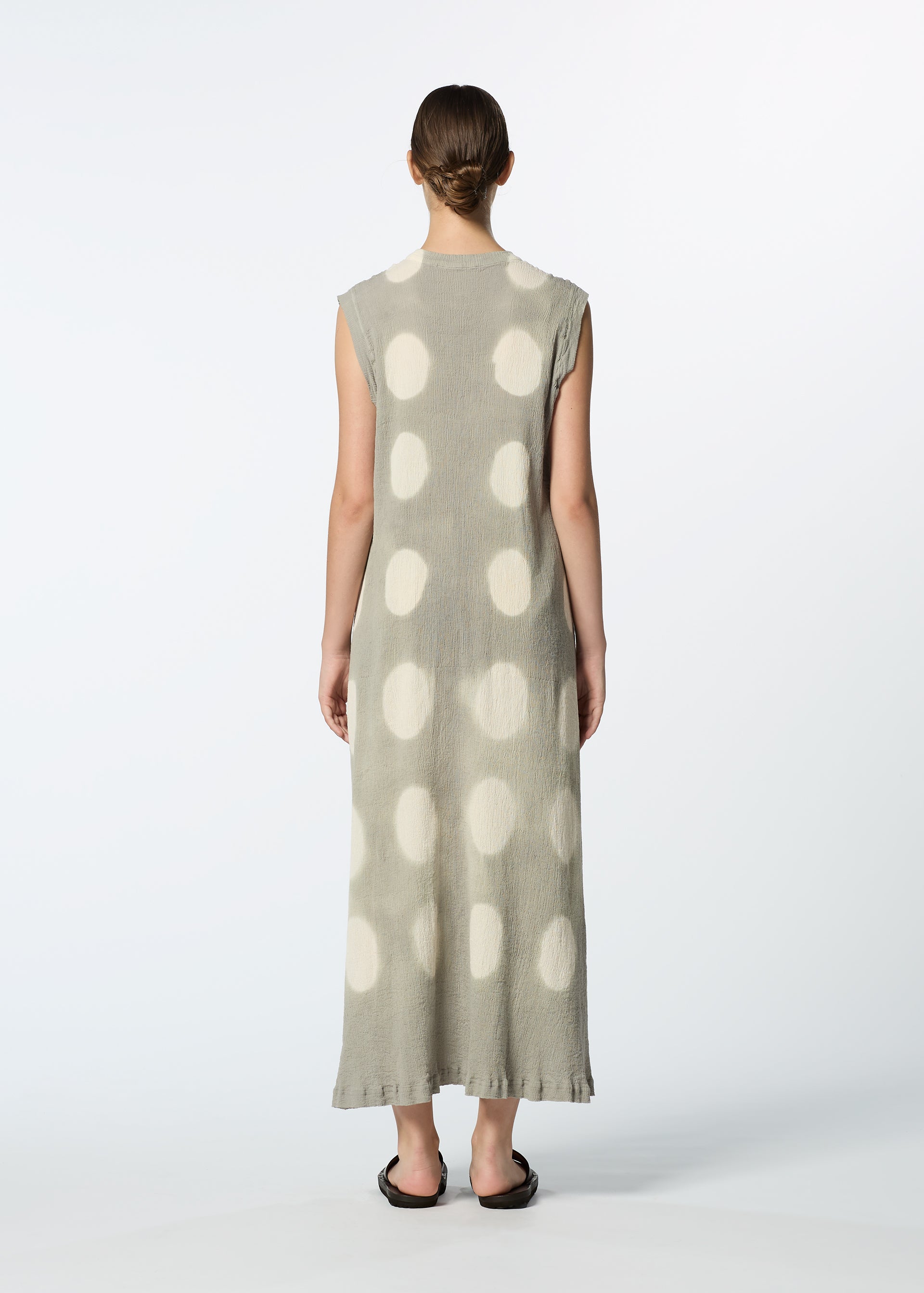 Zoomed view A person with short hair stands facing away, wearing the HaaT KYO CHIJIMI ITAJIME sleeveless, ankle-length handcrafted dress with large white polka dots and black sandals, photographed against a plain white background.