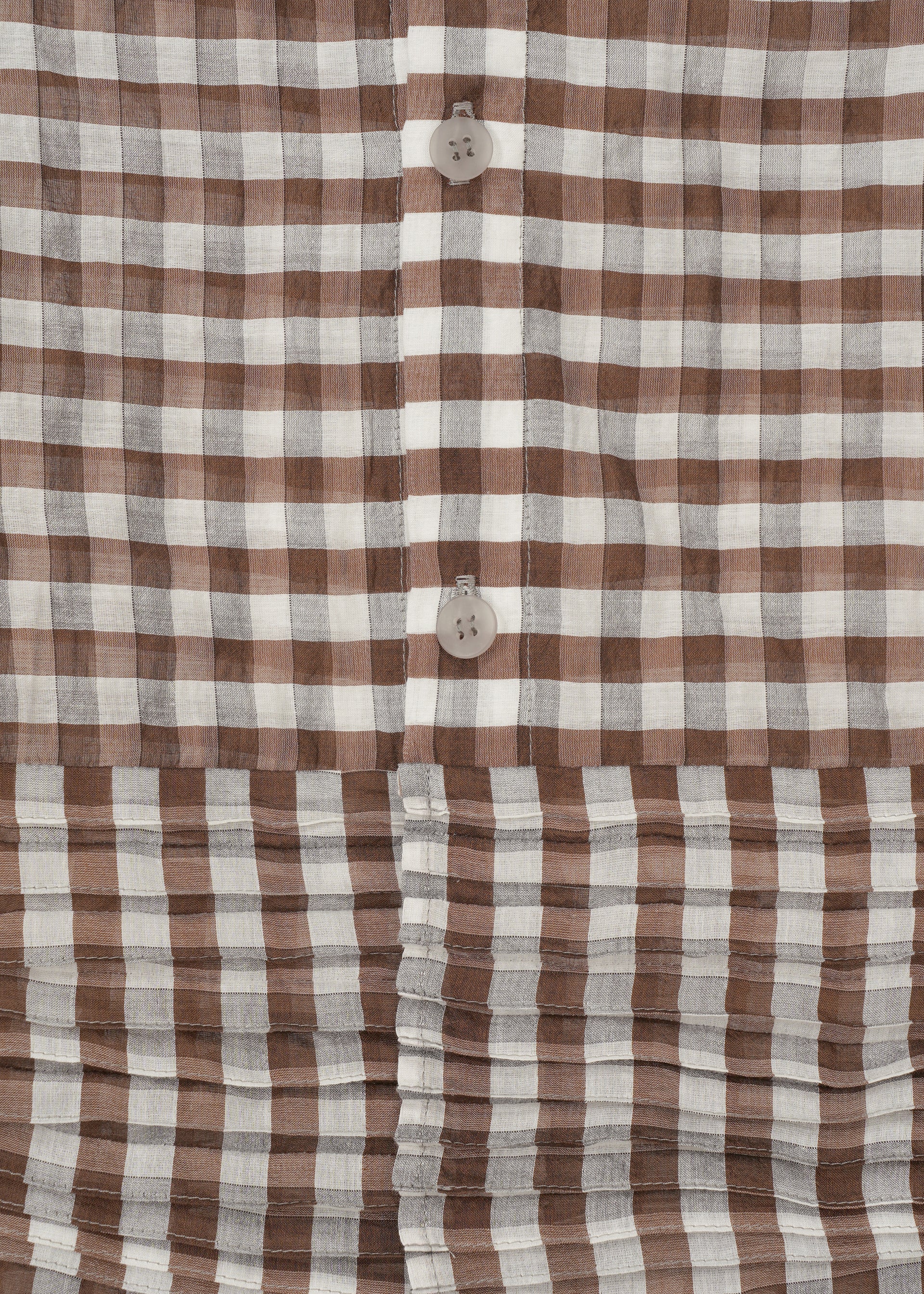 Zoomed view Close-up of HaaT's 2 SIDE PINTUCKING dress featuring a brown and white gingham pattern, vertical buttons, and horizontal pleats at the hem for a stylish contrast between smooth and pleated textures.