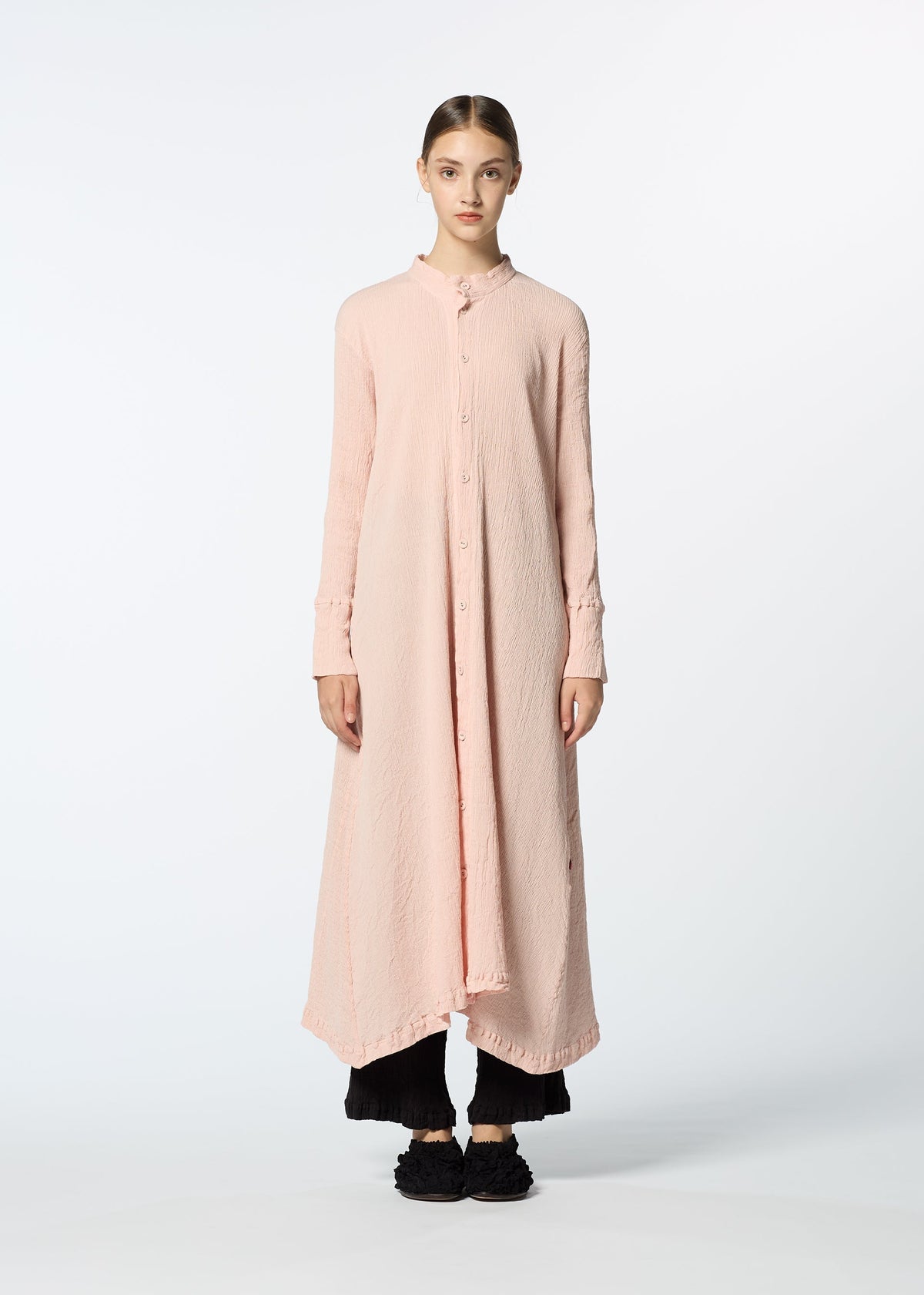 A person stands facing forward on a plain white background, wearing HaaT's KYO CHIJIMI FEBRUARY long-sleeved dress made from ultra-fine cotton yarn, paired with black wide-leg pants and black shoes. view 6 of 8