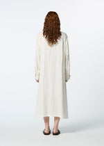 A person with long, curly hair is seen from behind wearing HaaT's JIKI, a loose, long-sleeved French linen dress, paired with black sandals against a plain white background.