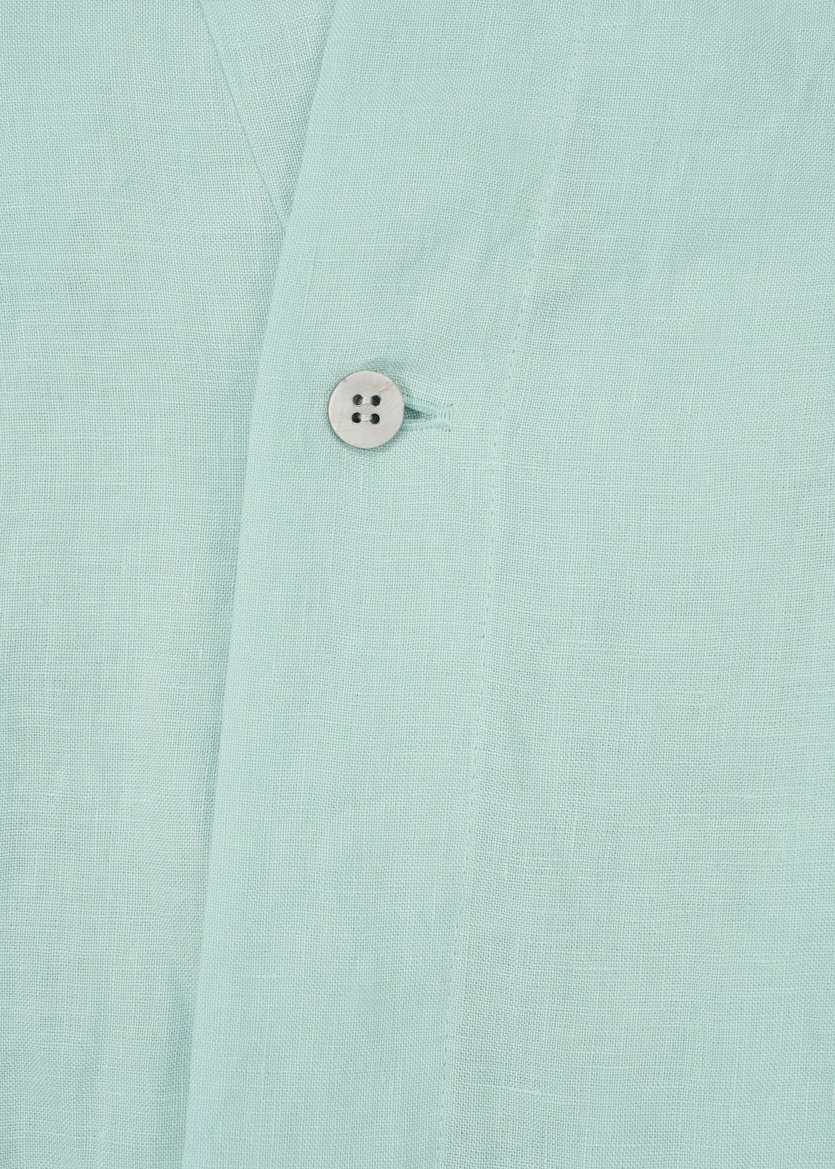 Close-up of JIKI by HaaT: light blue, breathable dress fabric featuring a visible seam and a single white button. The textured, linen-like material suggests an elegant silhouette and refined craftsmanship. view 5 of 9