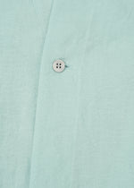 Close-up of JIKI by HaaT: light blue, breathable dress fabric featuring a visible seam and a single white button. The textured, linen-like material suggests an elegant silhouette and refined craftsmanship.