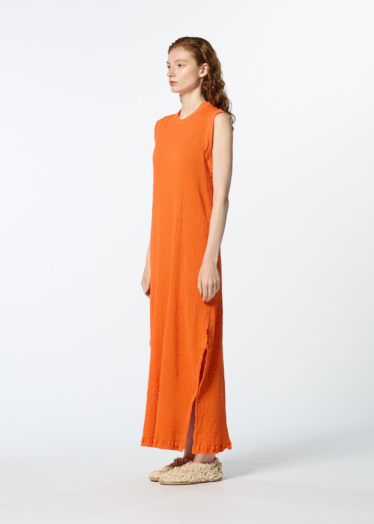 Against a white background, a woman wears the HaaT KYO CHIJIMI MAY sleeveless orange dress, crafted from ultra-fine cotton for lightweight comfort, paired with beige textured slip-on shoes as she faces slightly right. view 7 of 8