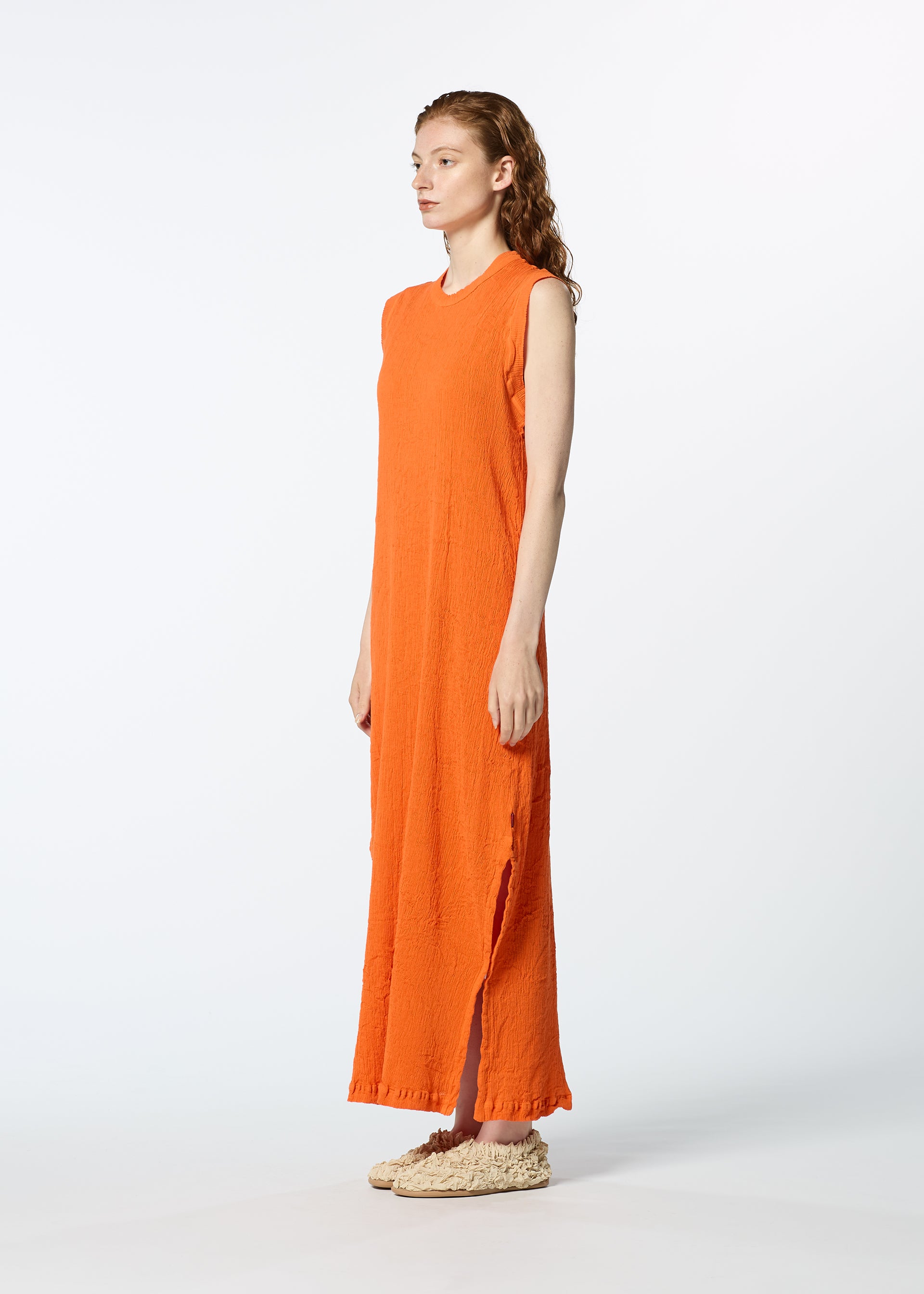Zoomed view Against a white background, a woman wears the HaaT KYO CHIJIMI MAY sleeveless orange dress, crafted from ultra-fine cotton for lightweight comfort, paired with beige textured slip-on shoes as she faces slightly right.