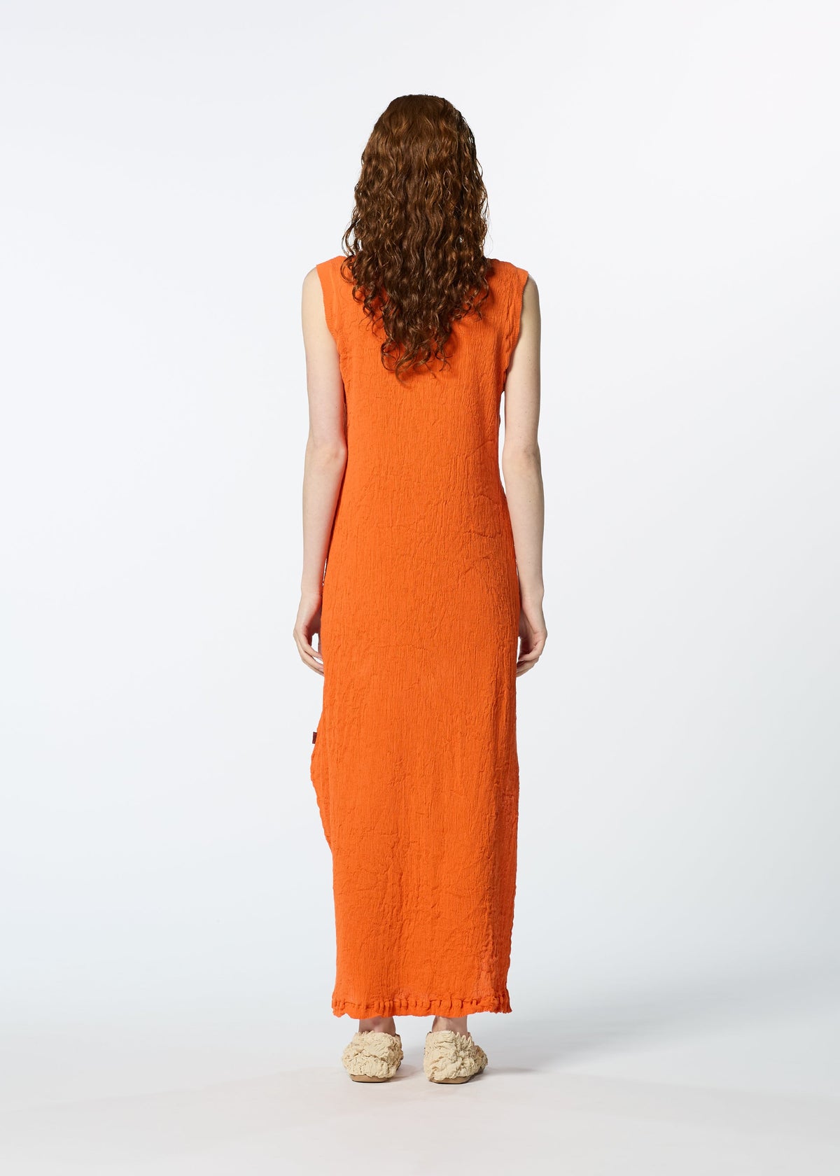 A person with long curly hair wears HaaT's KYO CHIJIMI MAY sleeveless dress, made from ultra-fine cotton yarn for a light and supple feel, and cream shoes, standing back to the camera against a plain white background. view 8 of 8