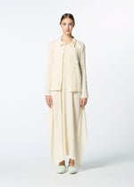 A woman stands facing forward in HaaT’s KYO CHIJIMI EMB set: an off-white, textured long jacket and matching wide ankle-length pants with subtle curved embroidery. Her hair is pulled back, and she wears soft slippers against a plain white background.