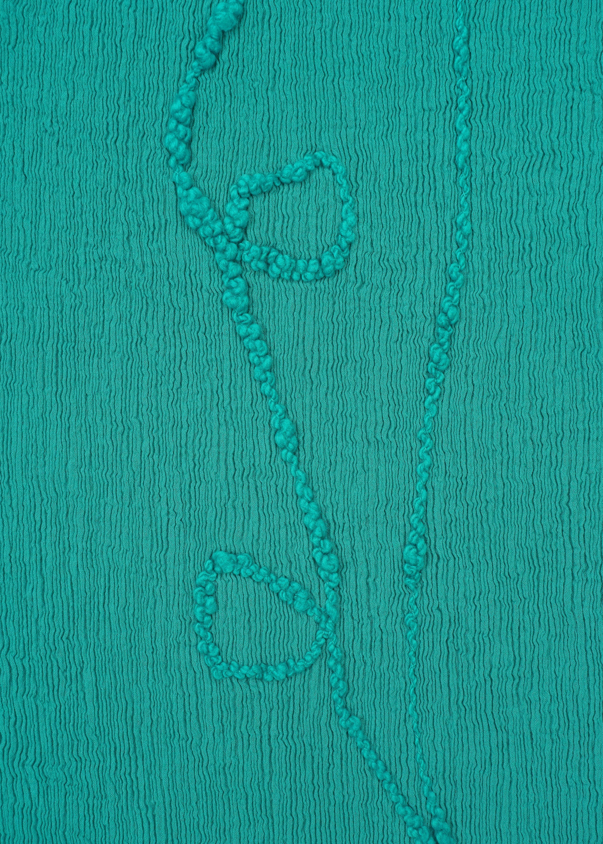 Zoomed view HaaT’s KYO CHIJIMI EMB features teal crinkled fabric with Garabo thread embroidery creating a vertical vine and three simple leaves.