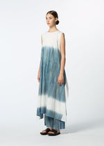A woman stands in a white studio wearing HaaT's SAZANAMI: a sleeveless, hand-painted organic cotton dress with blue and green vertical stripes, paired with coordinated wide-legged pants—reflecting refined Kyoto craftsmanship.