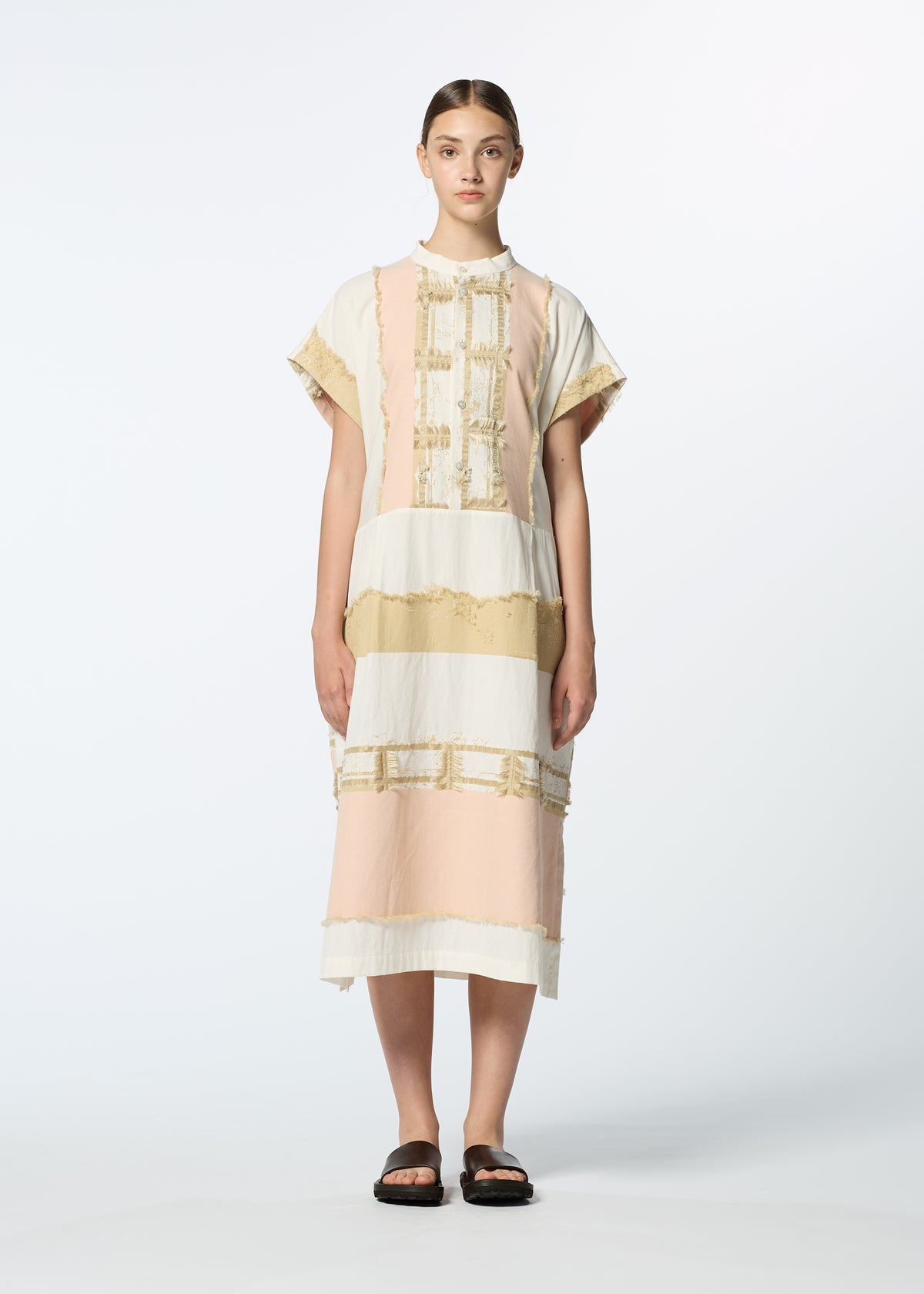 A person stands facing forward wearing the HaaT KASANEGAKE loose, knee-length jacquard dress with pastel pink, white, and beige horizontal stripes and short sleeves, paired with black sandals. The background is plain white. view 6 of 8