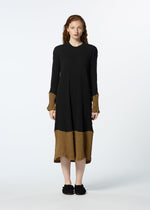A woman with wavy reddish-brown hair stands facing forward in a HaaT KYO CHIJIMI STREAM dress—black top, brown sleeves and hem—with black shoes, set against a plain white background.