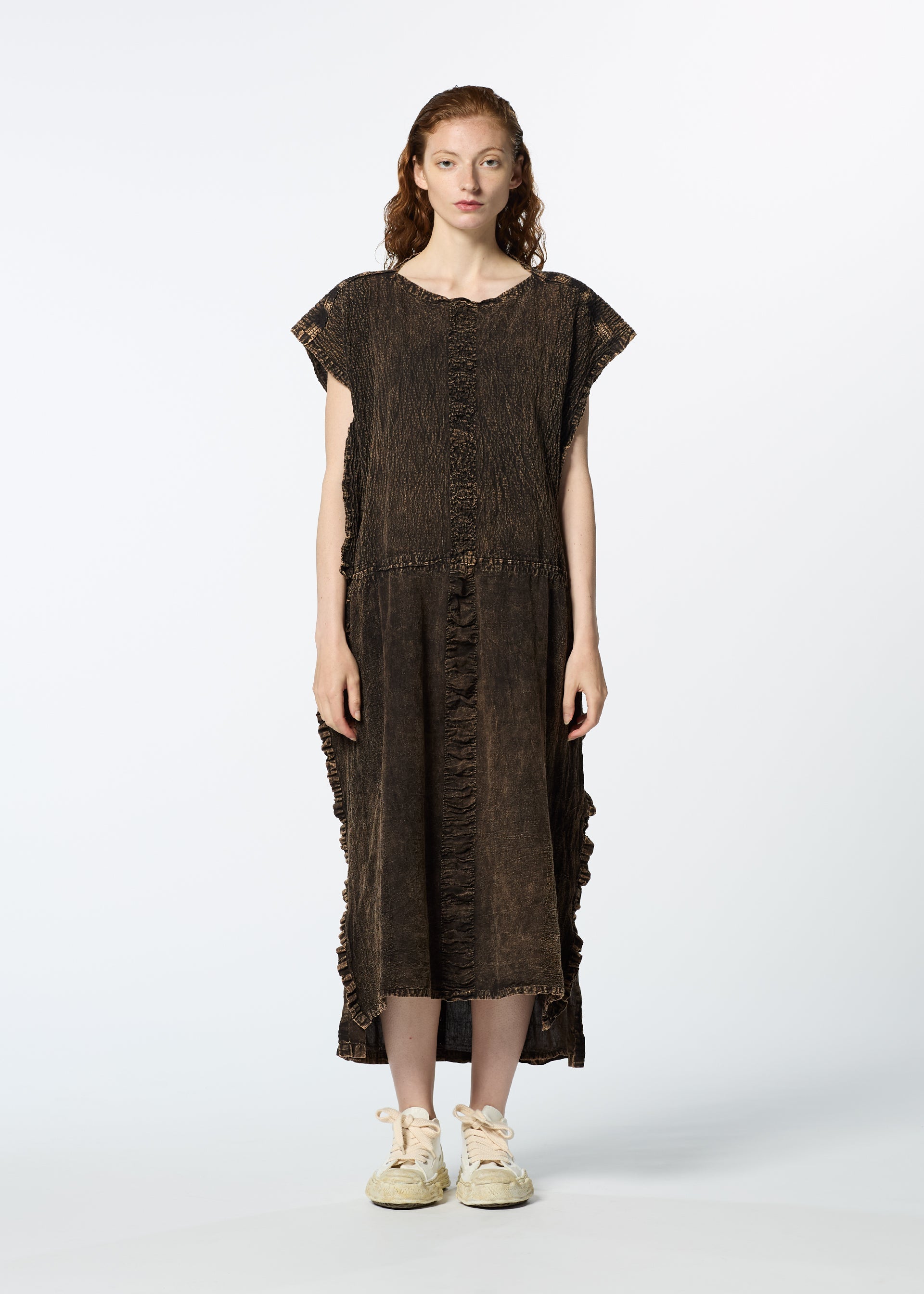 Zoomed view A woman with long, wavy brown hair wears the TENMOKU COTTON dress by HaaT, a loose, textured garment-dyed style with short sleeves and a ruffled hem. She stands facing forward against a white background with off-white sneakers.