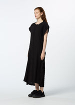 A person with long red hair stands sideways, wearing HaaT's TENMOKU COTTON—a loose-fitting black midi dress with a subtle mottled pattern inspired by Tenmoku glaze—paired with black sneakers, against a plain white background.