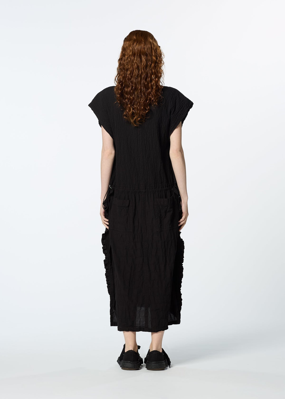 A person with long curly hair, dressed in a loose black HaaT TENMOKU COTTON dress featuring a subtle mottled pattern, stands facing away from the camera against a plain white background. view 7 of 7