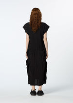 A person with long curly hair, dressed in a loose black HaaT TENMOKU COTTON dress featuring a subtle mottled pattern, stands facing away from the camera against a plain white background.